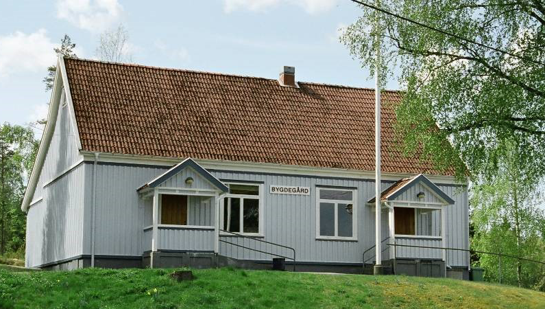 liten gråmålad byggnad med texten bygdegård på fasaden