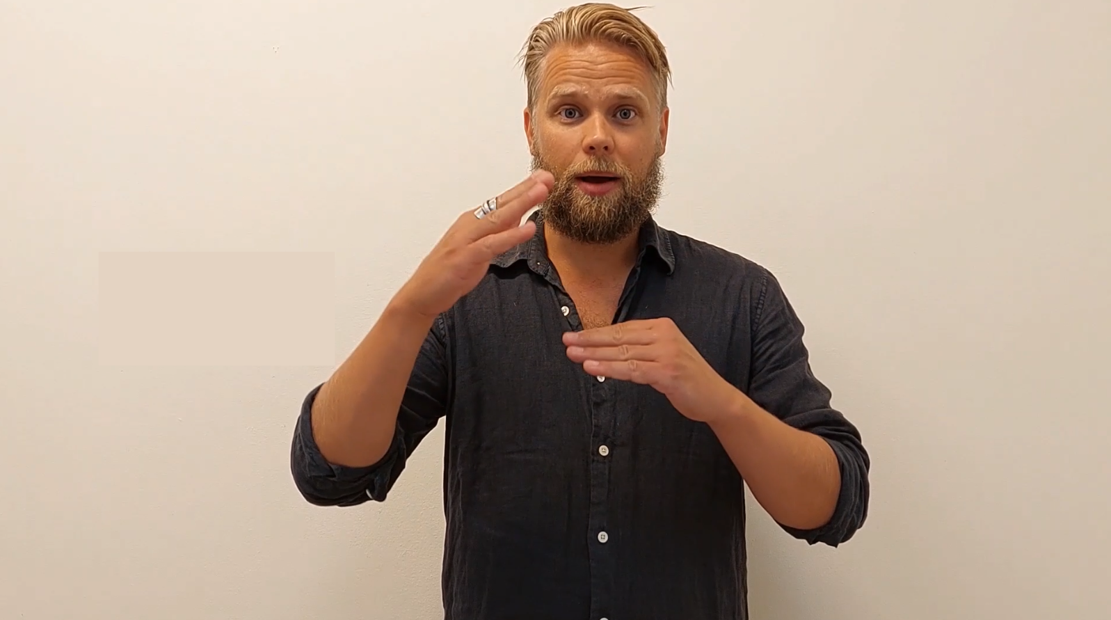 En man i mörk skjorta står mot en beige bakgrund och tecknar