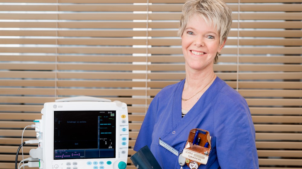 Blåklädd vårdpersonal står framför en jalousie, vid sidan av en apparat.