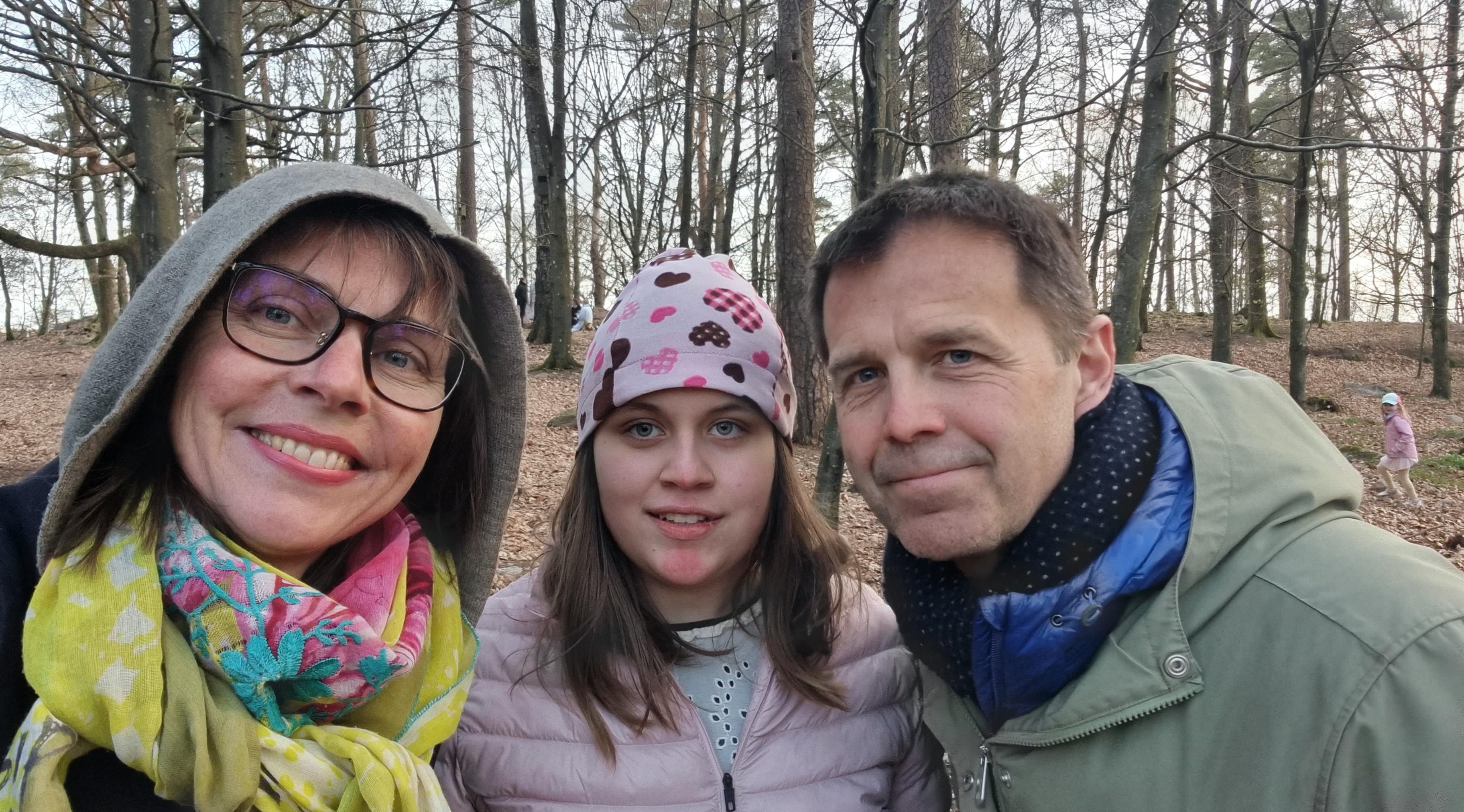 Tre personer, tjockare vinterkläder. Står framför träd som saknar löv