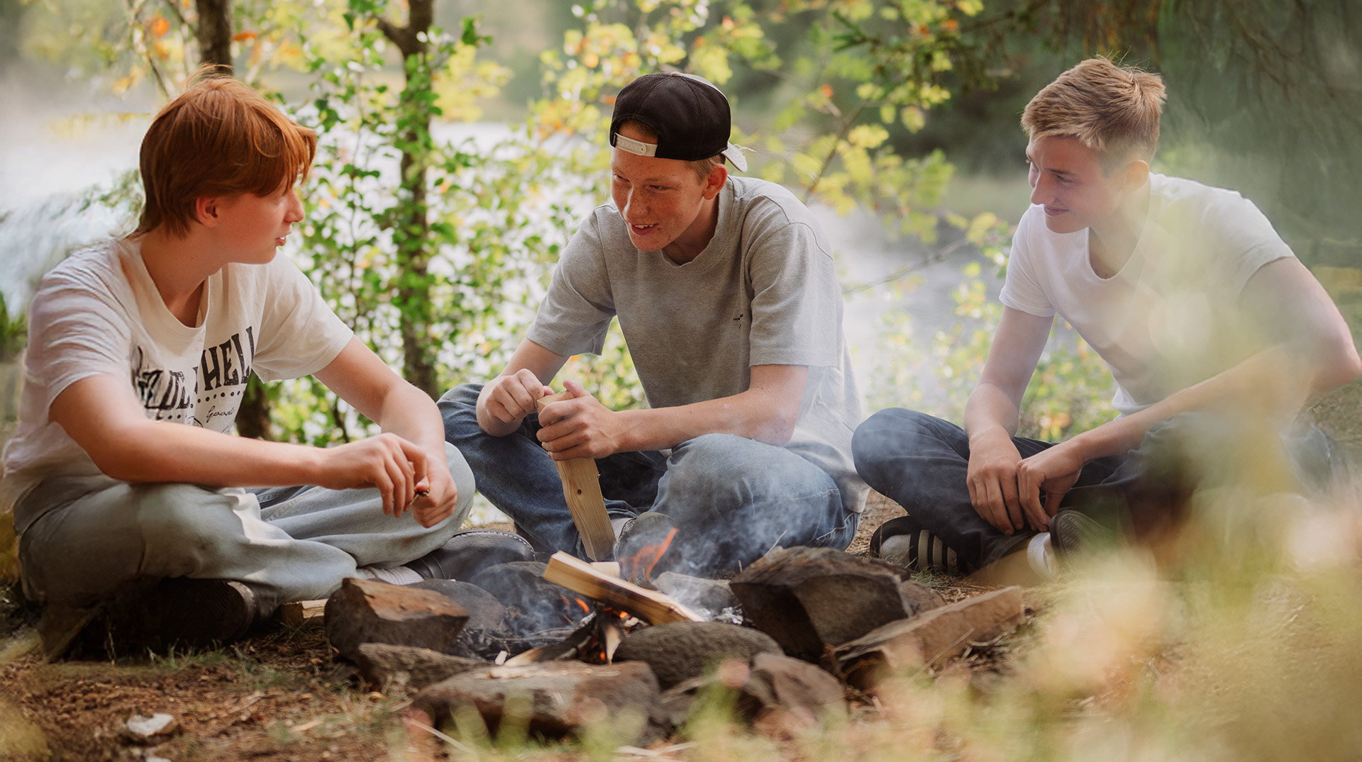 Tre elever sitter framför brasa i skogen